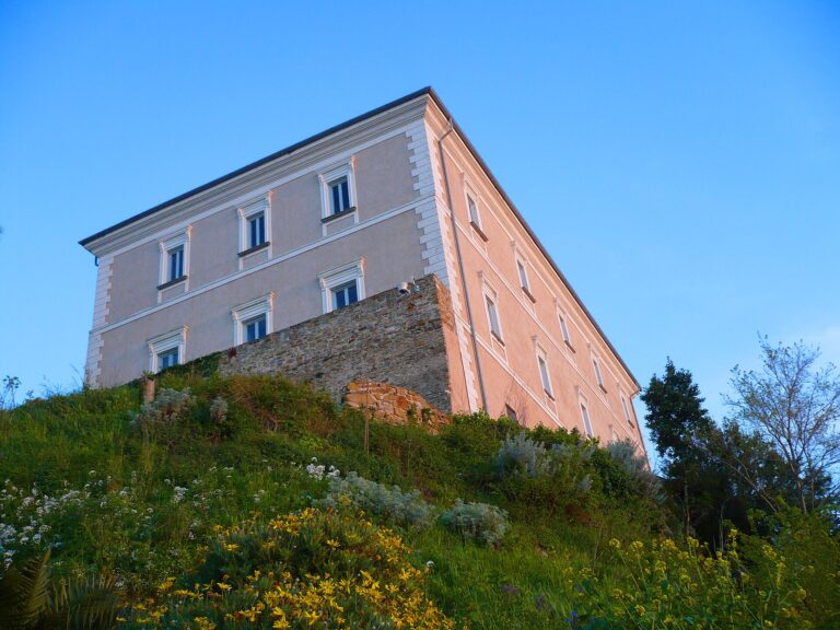 Il Castello dell'Abate a Castellabate: l'edificio chiaro a tre piani sopra le mura di pietra, sul colle coperto di erba e fiori gialli