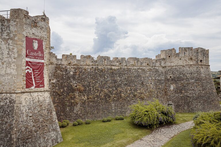 Le mura merlate del Castello di Agropoli con una torre d'angolo, il prato e il vialetto lungo il fossato