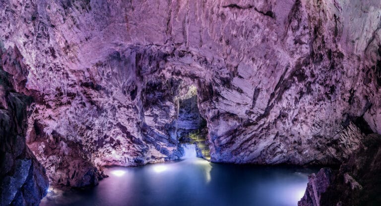 Sala delle Grotte di Pertosa-Auletta con la volta di roccia illuminata, un laghetto del fiume Negro e una piccola cascata