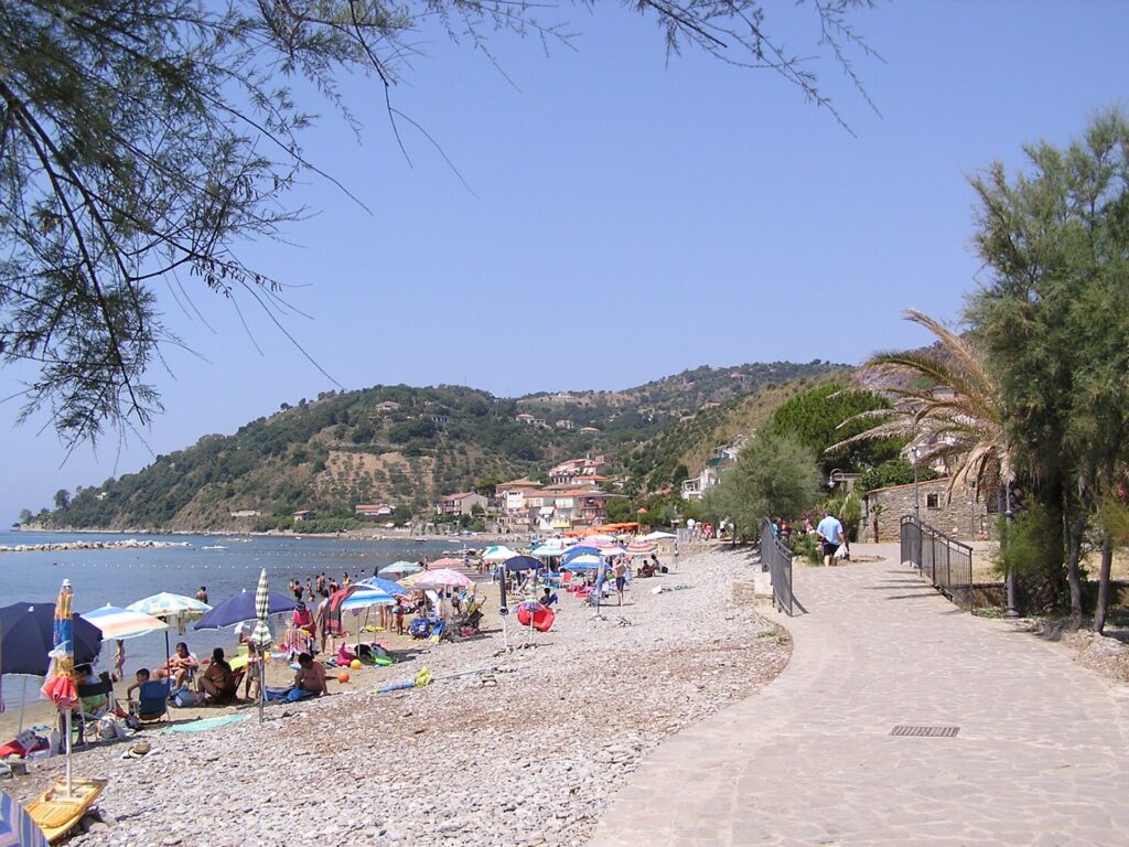 La spiaggia di ciottoli di Pioppi con gli ombrelloni, il lungomare e la collina verde sul mare